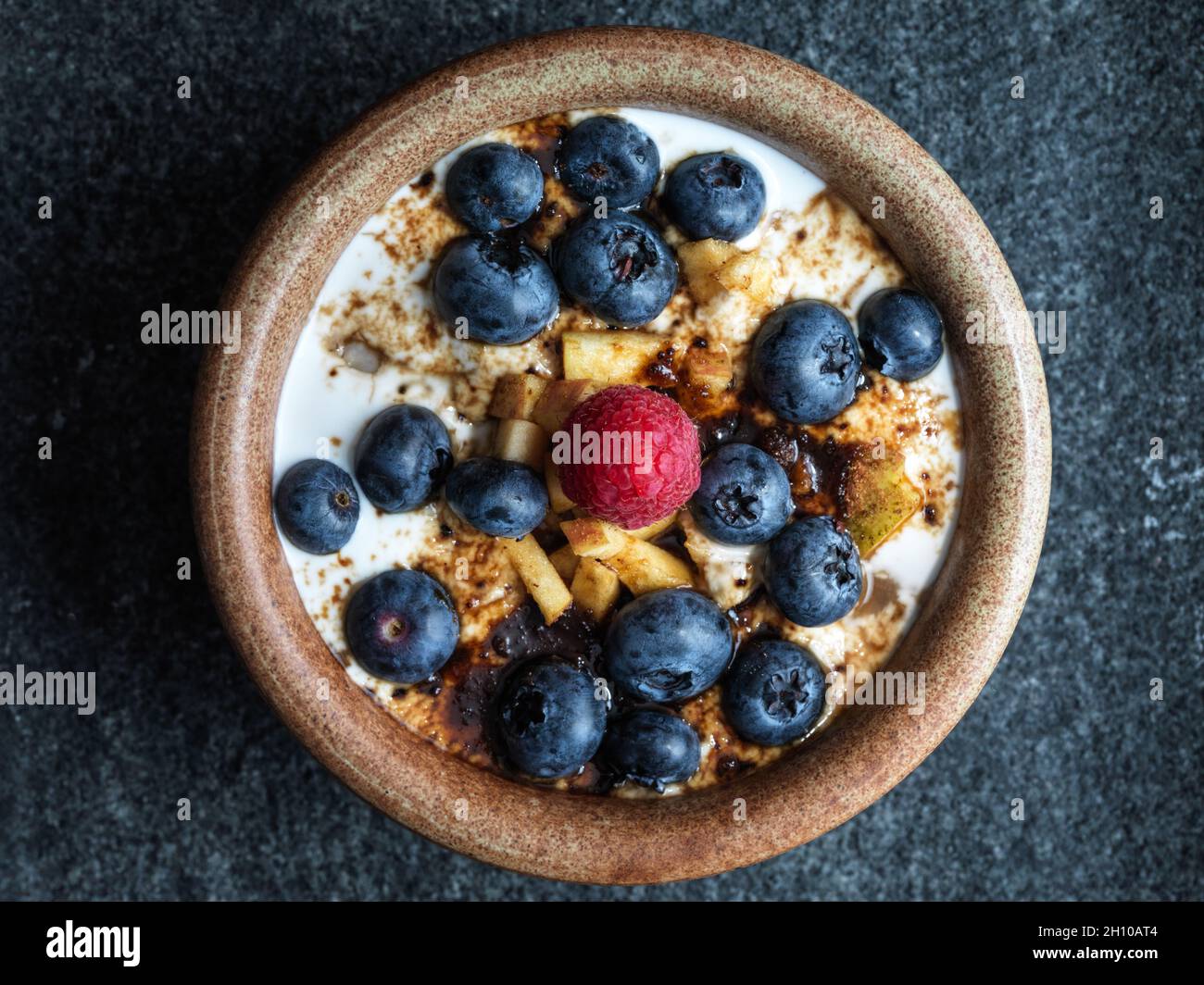 Gesundes Steel Cut Hafer Haferbrei Frühstück mit Apfel, Kokoscreme, blauen Beeren und Himbeere und einer Prise braunem Zucker Stockfoto