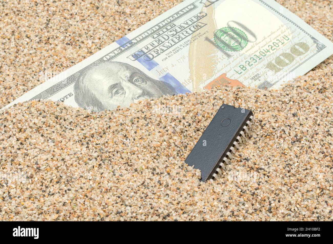 US-Banknote mit 100 US-Dollar/Banknote von Benjamin Franklin, vergraben in Sand mit Mikrochip. Für US-Halbleiterchip-Engpässe im Technologiesektor. Stockfoto