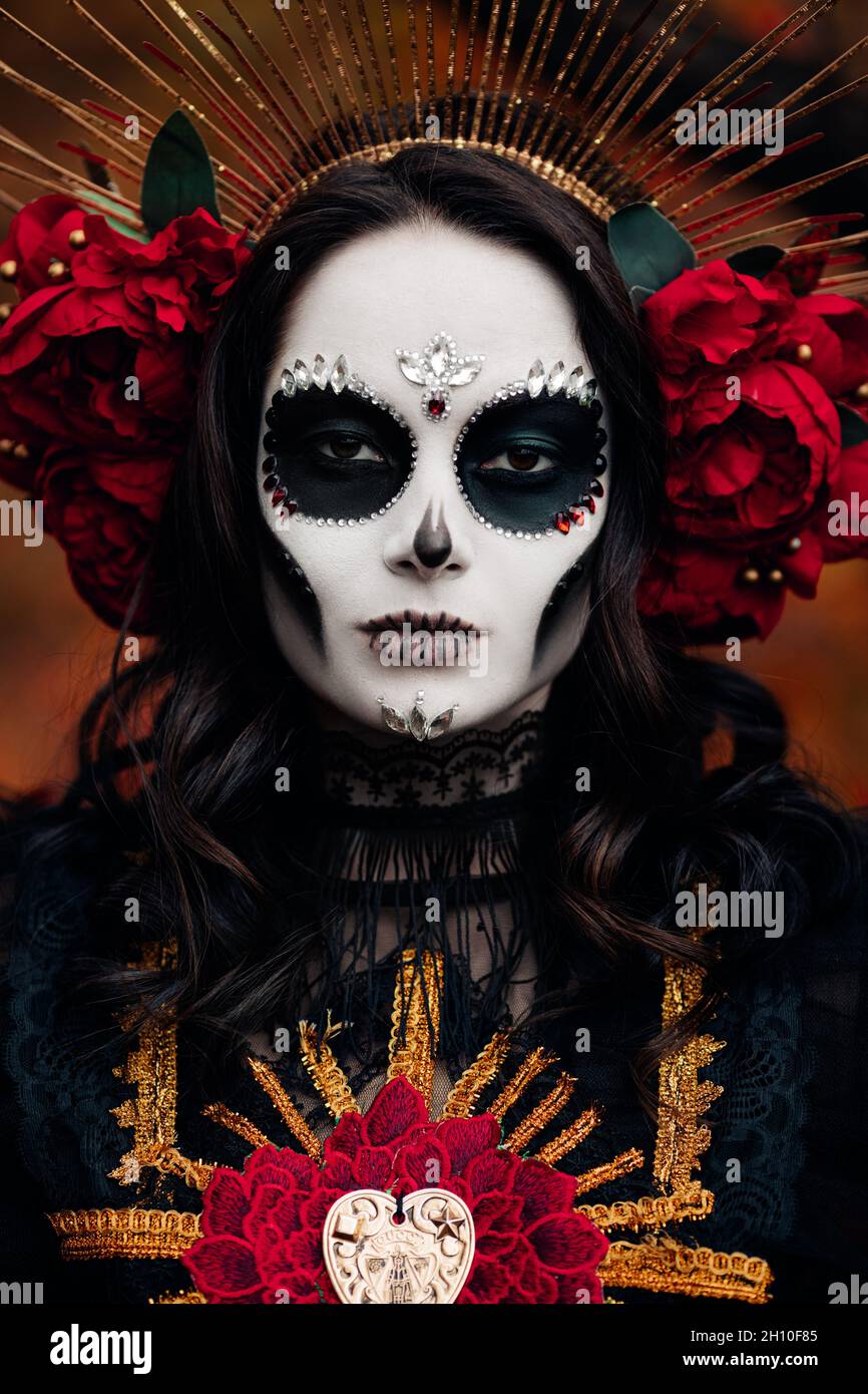 Porträt einer jungen Frau mit Totenschädel-Make-up und roten Rosen in schwarzem Todeskostüm als Santa Muerte. Tag der Toten oder Halloween-Konzept. Stockfoto