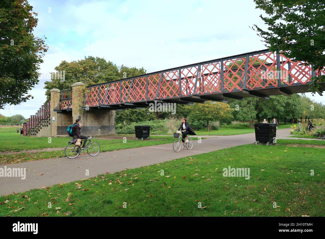 Burgess Park, Peckham, London, Großbritannien. Radfahrer und Fußgänger auf einem Weg entlang der alten Surrey Canal Route. Zeigt die originale viktorianische Kanalbrücke. Stockfoto