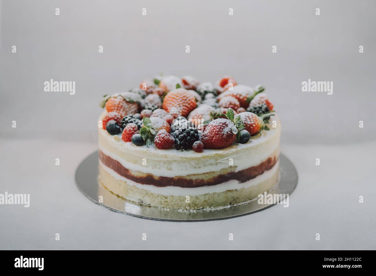 Köstlicher weißer Kuchen mit natürlichen Früchten und weißem Pulver auf weißem Hintergrund. Schöne leckere süße Dessert mit mehreren Schichten Stockfoto