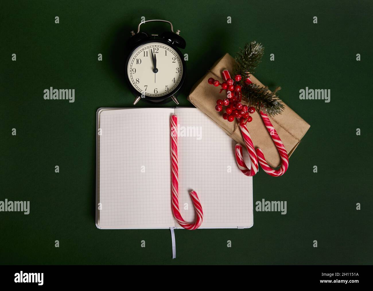 Hochwinkelansicht des Weckers mit Mitternacht, Weihnachtsgeschenk in Geschenkpapier, Stechpalme, Zuckerstöcke und Notizblock mit geöffneter Seite verpackt Stockfoto