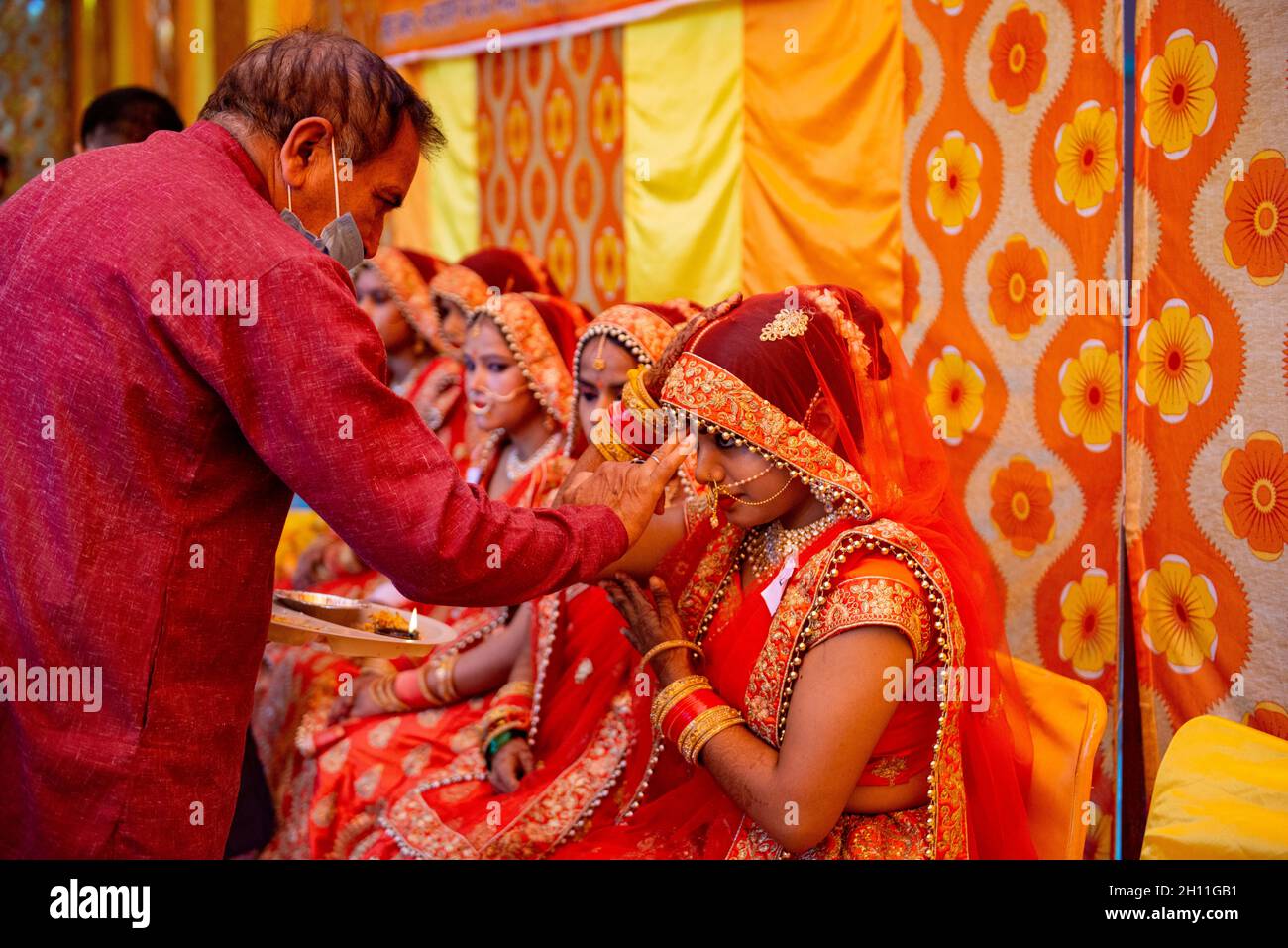 Neu-Delhi, Indien. Oktober 2021. Priester in Maske, der Tilak (hinduistisches Sakralzeichen) während des Hochzeitsrituals auf die Stirn der Braut aufträgt. Lions Club Delhi Karan organisierte eine Samuhik Viva (Massenhochzeit) für wirtschaftlich schwächere Gebiete in Sarva Sanatan Shiv Mandir, Trilokpuri. Kredit: SOPA Images Limited/Alamy Live Nachrichten Stockfoto