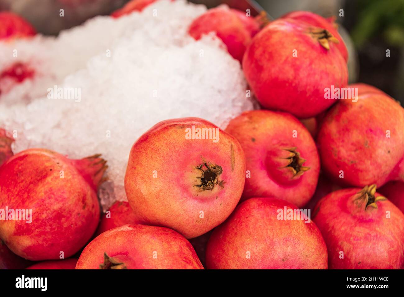 Granatäpfel liegen auf einem Marktstand. Rote Granatapfelfrüchte und Eis, um sie frisch zu halten. Stockfoto