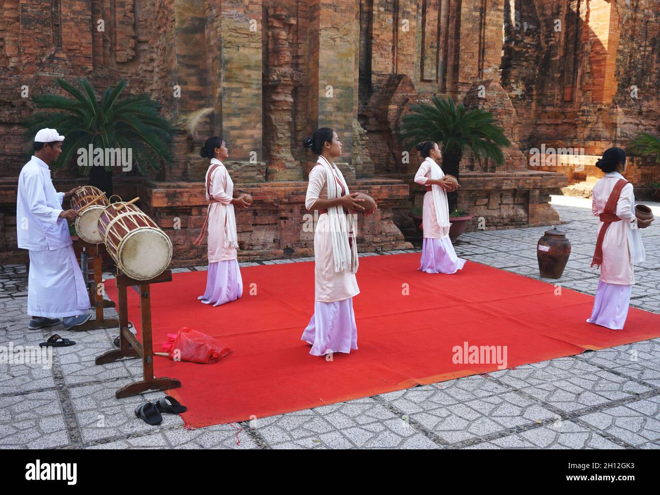 Junge vietnamesische Frauen, begleitet von einem Schlagzeuger, führen einen traditionellen ethnischen Tanz neben dem alten Po Nagar Cham Tempel in Nha Trang, Vietnam, auf Stockfoto