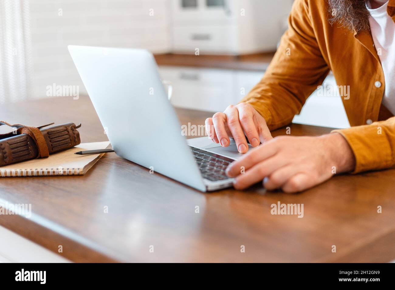 Mann verwenden Laptop für Online-Ausbildung oder Einkaufen. Nahaufnahme männliche Hände junger Mann, der von zu Hause aus am Laptop in der Küche zu Hause arbeitet. Freiberufler Stockfoto