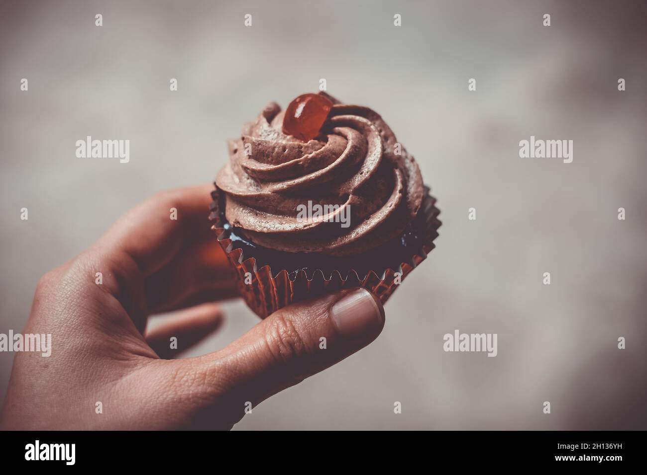 Hand hält einen leckeren Schokoladenkuchen mit süßem cremigem Spiralfrosting und Kirschscheiben-Belag. Selektiver Fokus. Persönliche Perspektive. Stockfoto
