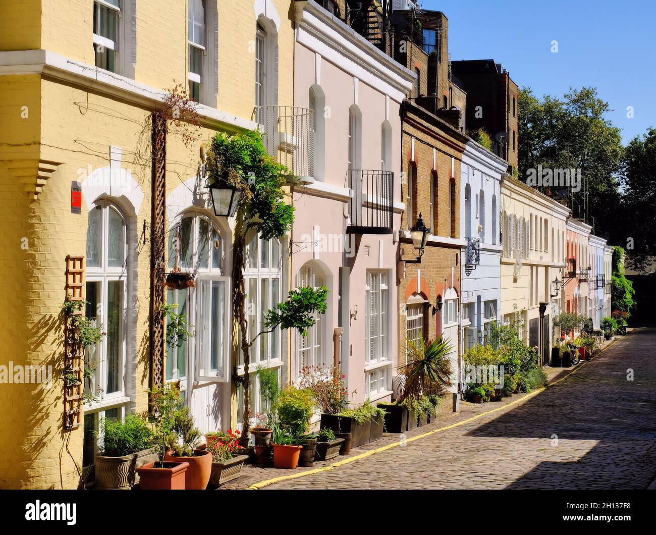 Farbenfrohe und sonnige Häuser und Blumen in der Kopfsteinpflasterstraße Ennismore Garden Mews, Knightsbridge, London, England Stockfoto
