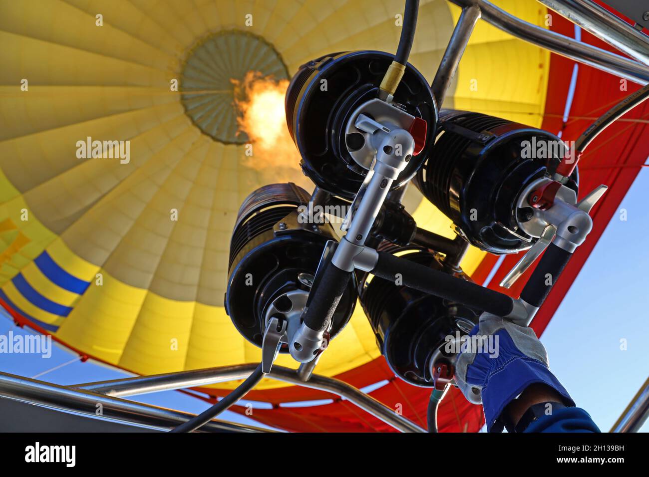 Heißluftballon-Pilot hat seine Hand auf dem Gasbrenner und füllt heiße Luft in einen gelben Ballon Stockfoto