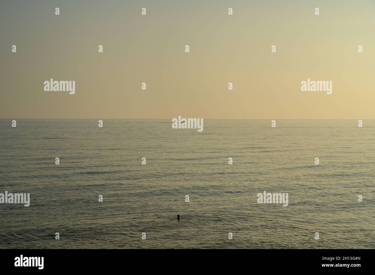 Ein einsamer Schwimmer und ein Motorboot in Silhouette vor dem ruhigen Meer in glühendem Oktobernachmittagssonne vor Hove Beach, East Sussex, England. Stockfoto