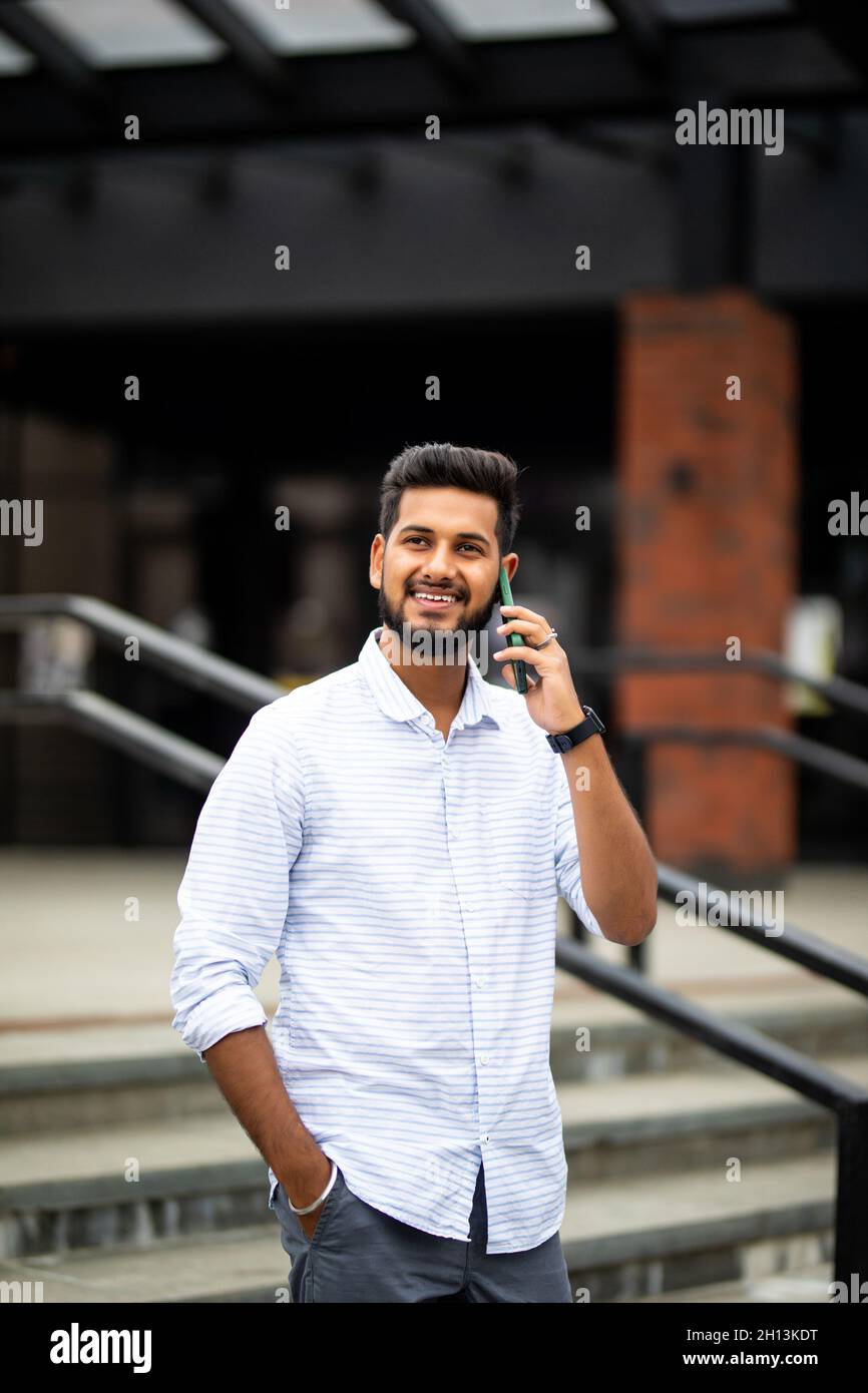 Schön lächelnden jungen Mann verkleidet beiläufig die Zeit im Freien in der Stadt, mit Handy, während die Treppe hinunter. Stockfoto