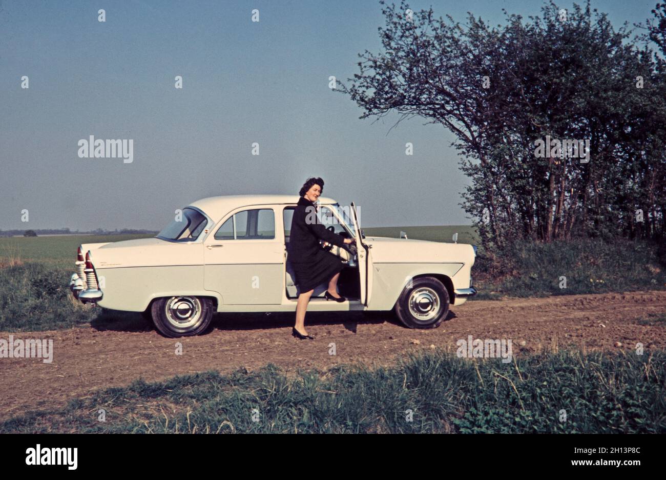 Ein Vintage-Farbfoto aus dem Jahr 1959, das eine Frau zeigt, die bei einem Ford Zodiac steht. Sie hat einen Fuß in die Fahrerseite des Autos. Aufgenommen in Suffolk England. Stockfoto