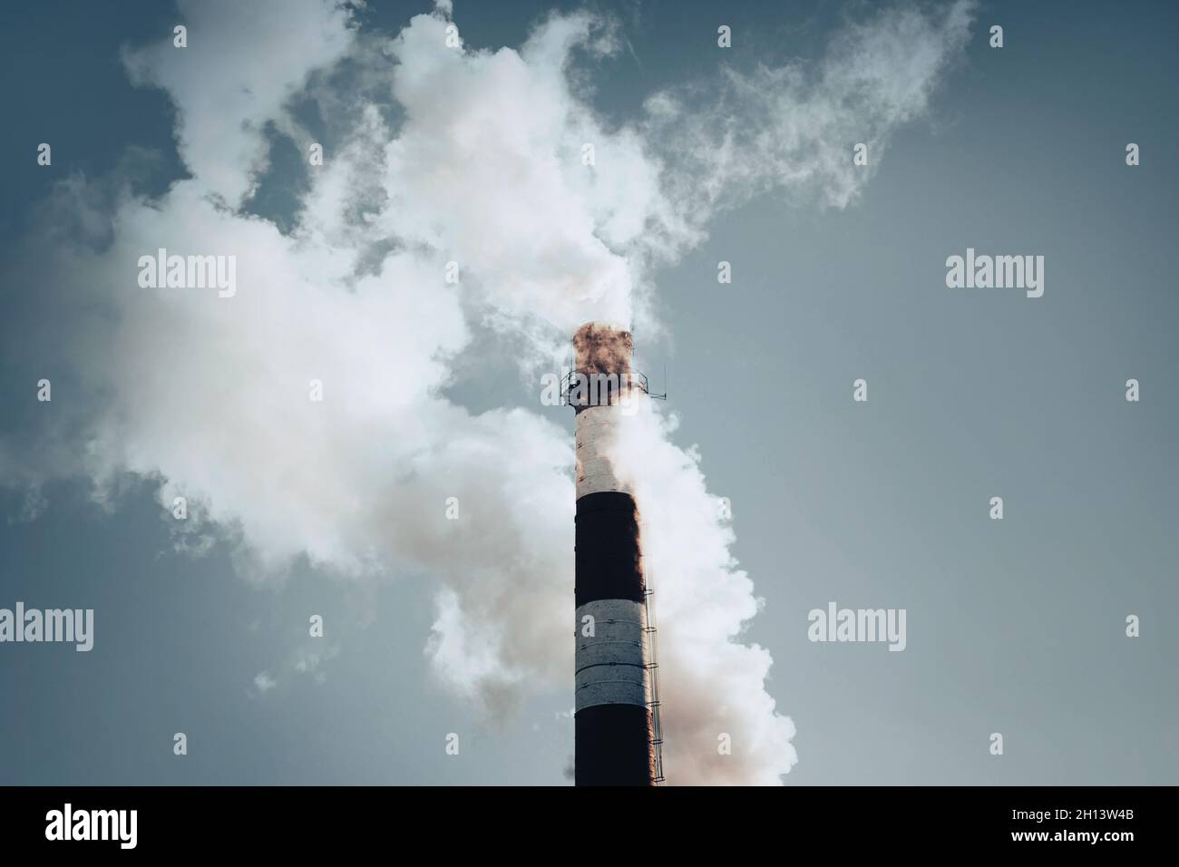 Das gestreifte Rohr der Pflanze, das umweltschädlichen Rauch in den blauen Himmel ausgibt. Der Ökologie der Erde Schaden zufügen. Schädliche Emissionen. Stockfoto