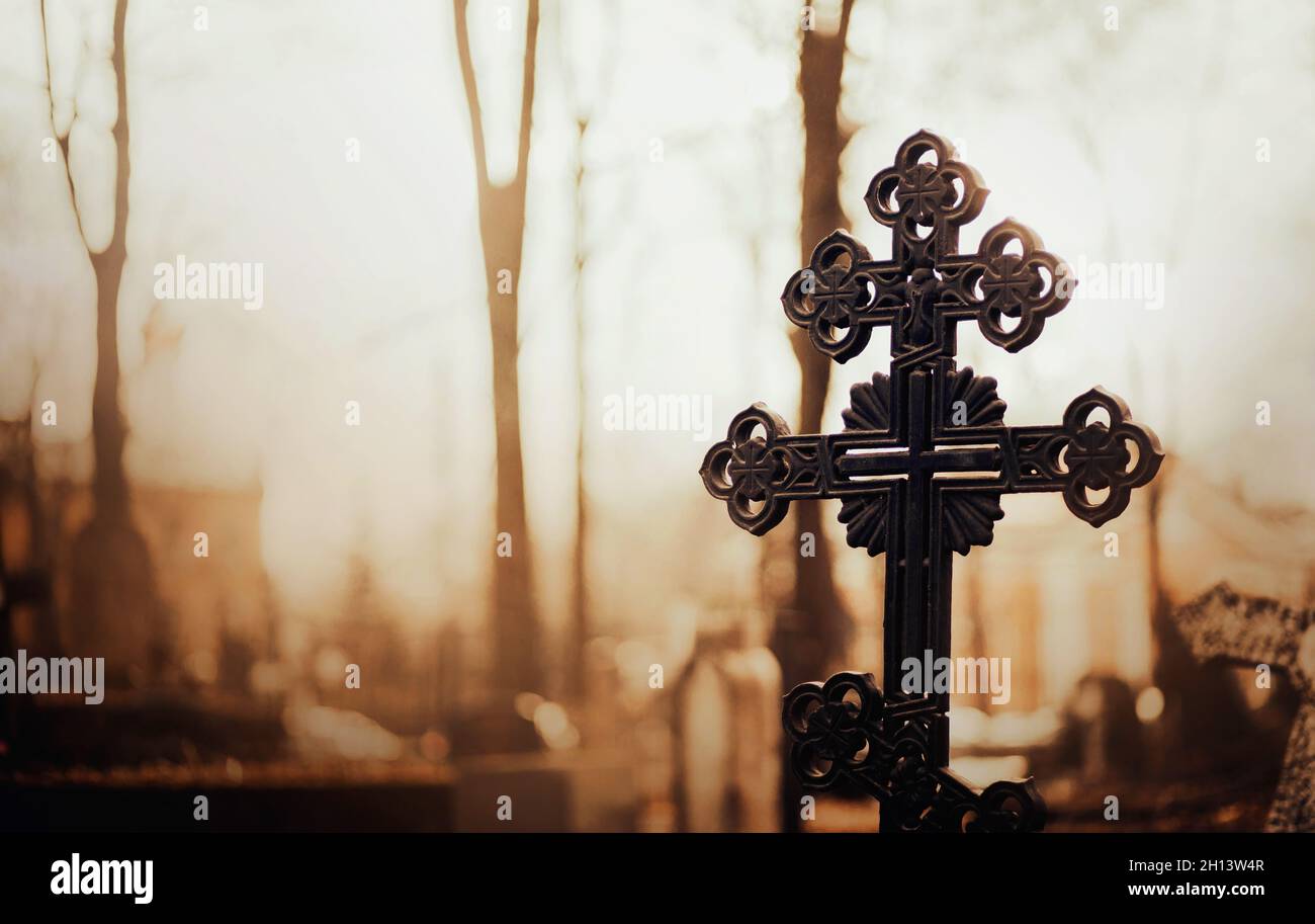 Ein schönes schwarzes altes Kreuz auf dem Friedhof am Morgen wird von den Strahlen der aufgehenden Sonne beleuchtet. Religion. Stockfoto