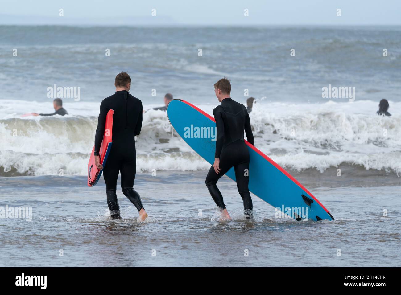 Zwei Surfer gehen in die Wellen von Croyde Bay, North Devon, Großbritannien. Stockfoto