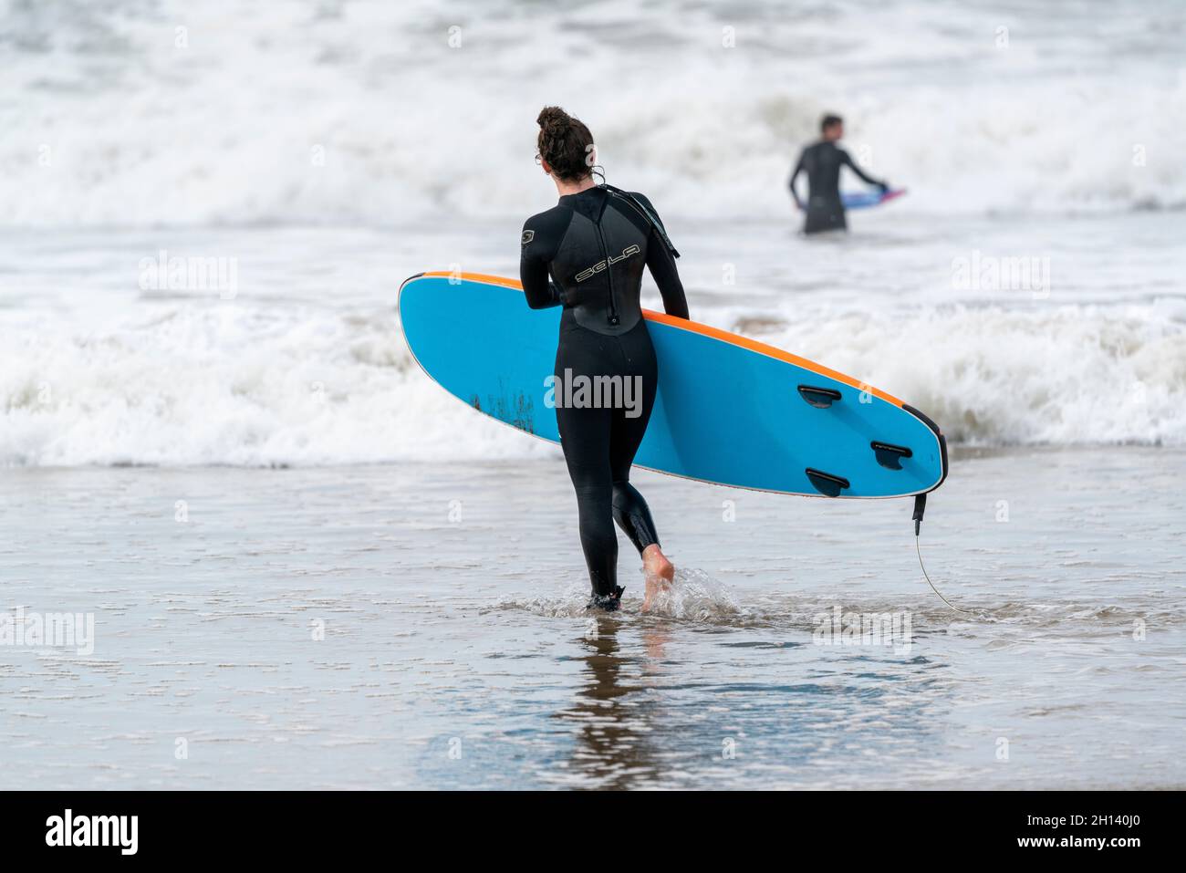 Eine Surferin geht in die Wellen von Croyde Bay, North Devon, Großbritannien. Stockfoto