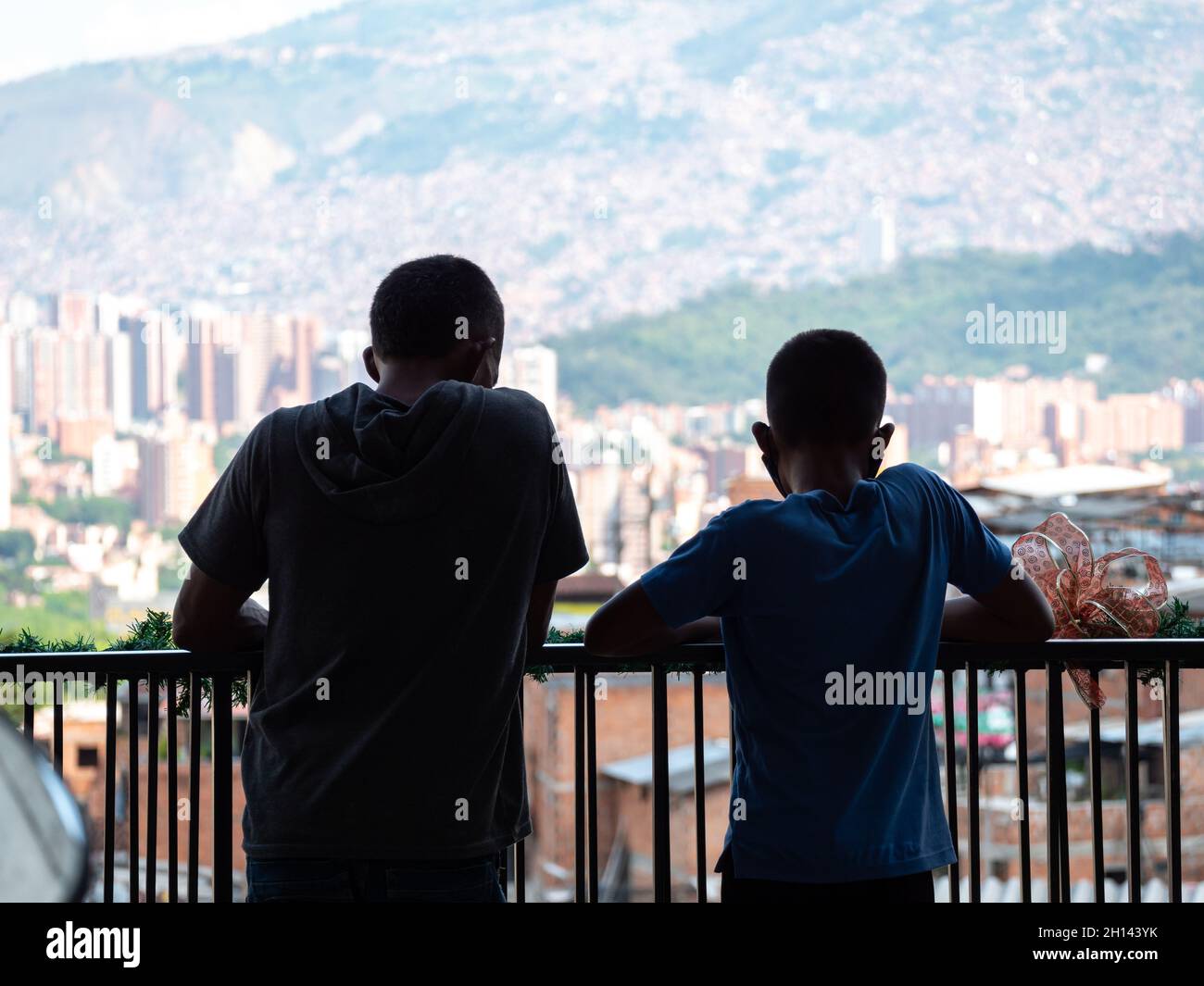 Kinder, die auf dem Geländer einer Terrasse schwellen und den Blick auf die Kommune 13, ein Touristenviertel in Medellin, Kolumbien, betrachten Stockfoto