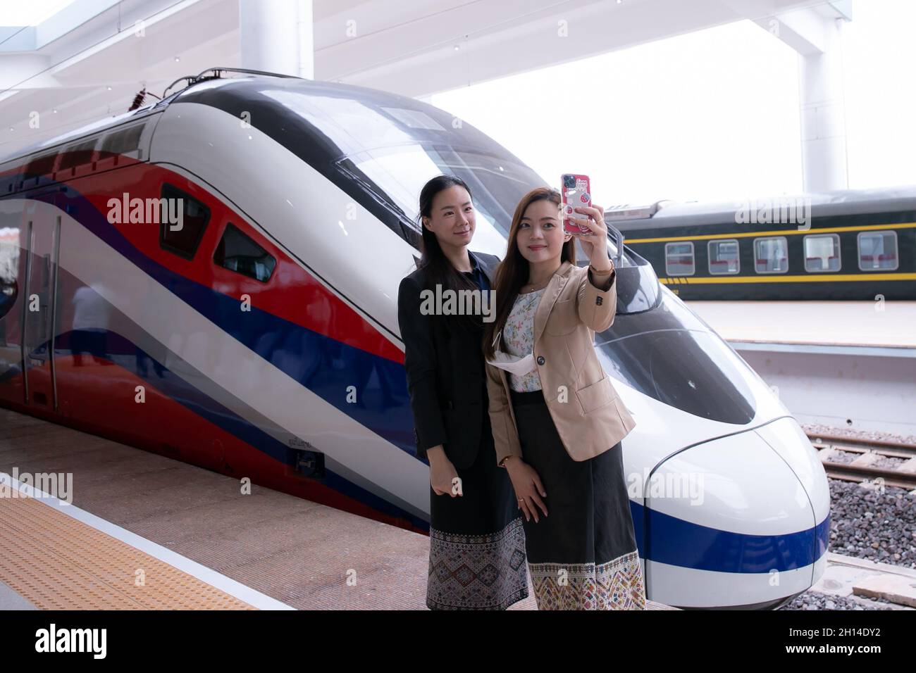 Vientiane, Laos. Oktober 2021. (211016) -- VIENTIANE, 16. Oktober 2021 (Xinhua) -- zwei Frauen posieren für Fotos mit dem Lane Xang EMU-Zug am Bahnhof Vientiane in der laotischen Hauptstadt Vientiane, 16. Oktober 2021. Der stromlinienförmige Hochgeschwindigkeitszug, kurz EMU, für die China-Laos-Eisenbahn, kam am Samstag auf dem neu erbauten Bahnhof Vientiane der China-Laos-Eisenbahn an. Der EMU-Zug wurde offiziell an die Laos-China Railway Co., Ltd. Geliefert, ein Joint Venture mit Sitz in der laotischen Hauptstadt Vientiane, das für den Bau und Betrieb der Eisenbahn verantwortlich ist Stockfoto