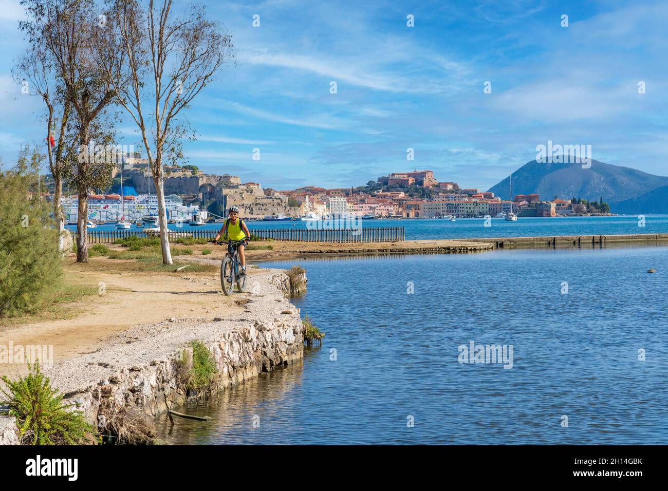 Nette Frau, die mit ihrem elektrischen Mountainbike an der Küste des mittelmeers auf der Insel Elba im toskanischen Archipel, vor Porto, fährt Stockfoto
