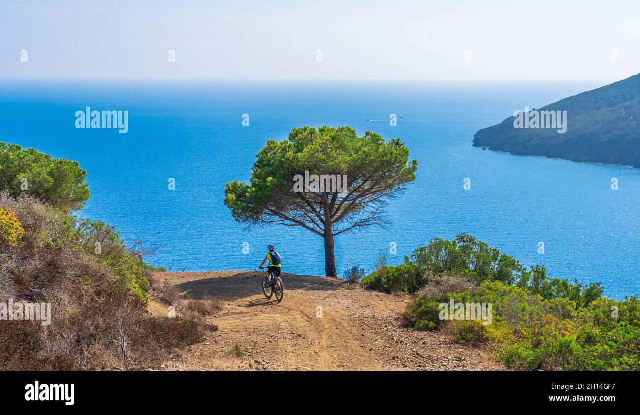 Nette Frau, die mit ihrem elektrischen Mountainbike an der Küste des mittelmeers auf der Insel Elba im toskanischen Archipel, vor Porto, fährt Stockfoto