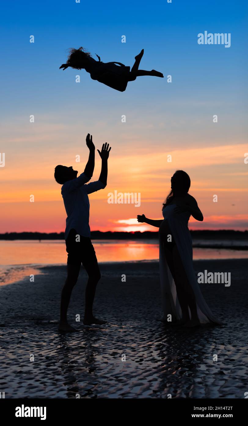 Vater Silhouette mit seiner Schwangeren Frau, wirft sein Kind in die Luft bei Sonnenuntergang auf dem Meer Stockfoto