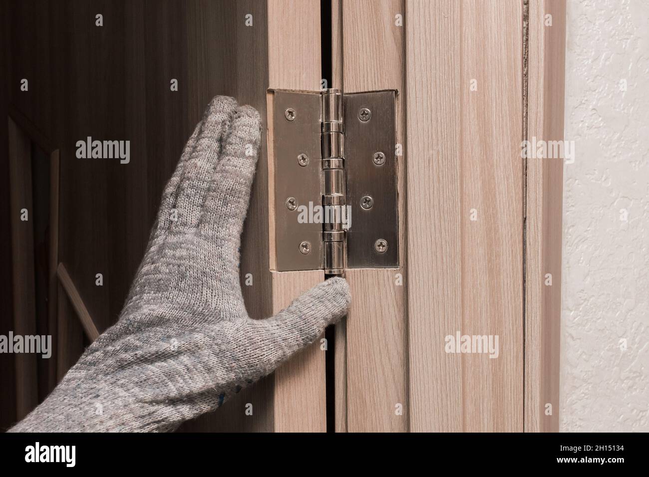Die Hand eines Arbeiters in einem Bauhandschuh berührt und untersucht eine hölzerne Türöffnung mit einem Türscharnier, Nahaufnahme. Einbau oder Einstellung o Stockfoto