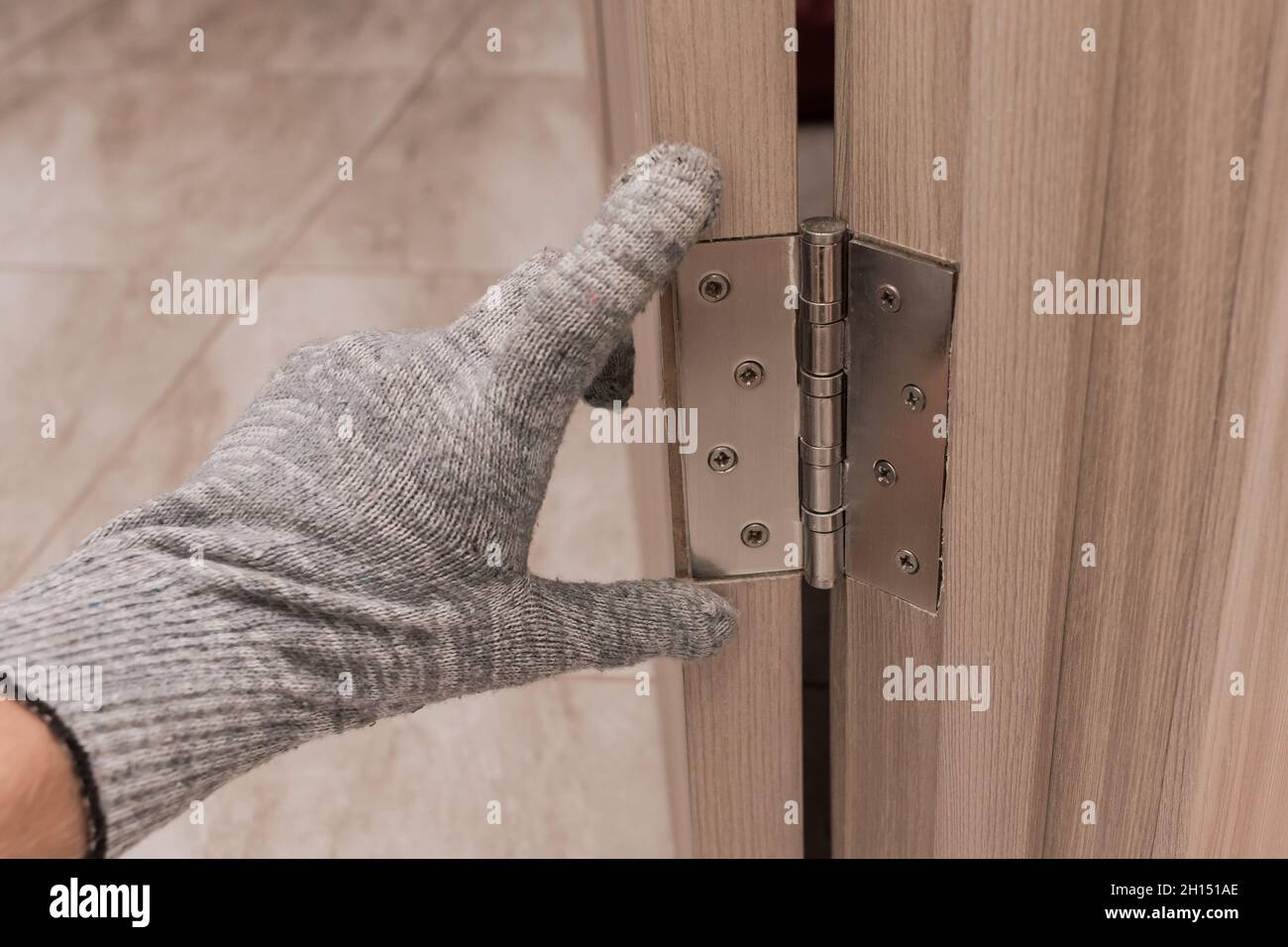 Die Hand eines Arbeiters in einem Bauhandschuh berührt und untersucht eine hölzerne Türöffnung mit einem Türscharnier, Nahaufnahme. Einbau oder Einstellung o Stockfoto