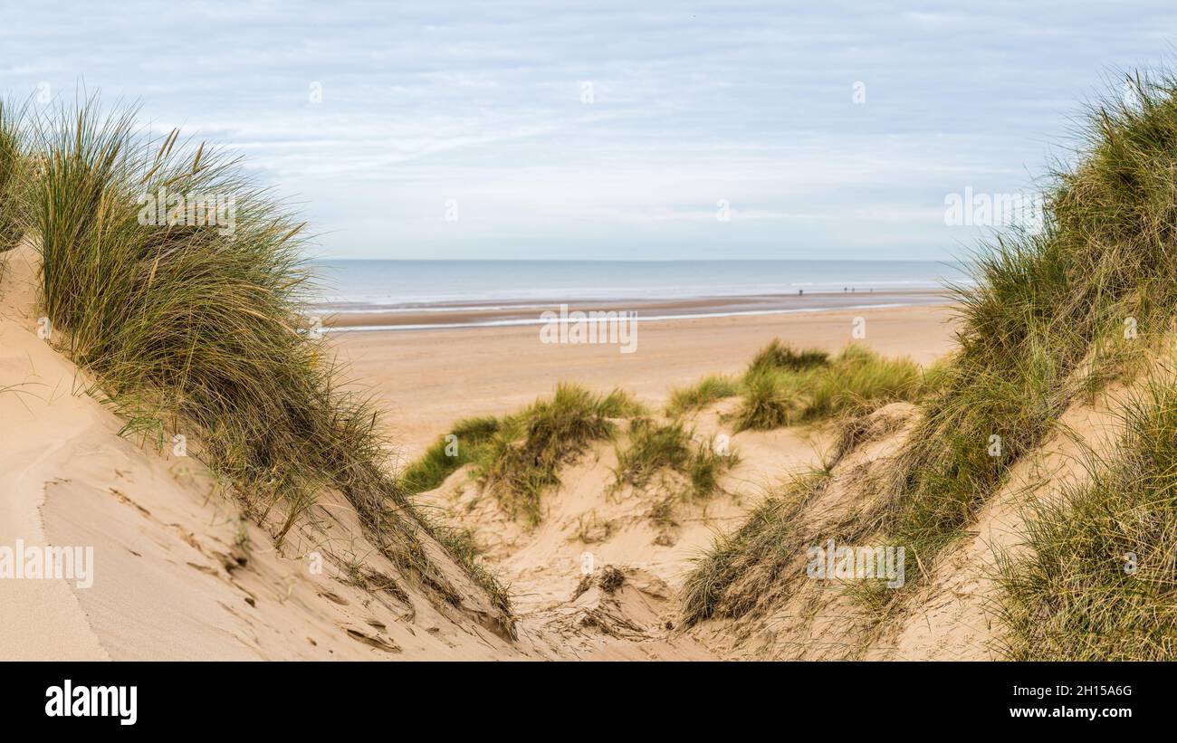 Ein Panorama aus mehreren Bildern, das zwischen zwei Gipfeln auf den Sanddünen aufgenommen wurde und auf Menschen blickt, die am Strand von Formby in der Nähe von Liverpool spazieren. Stockfoto