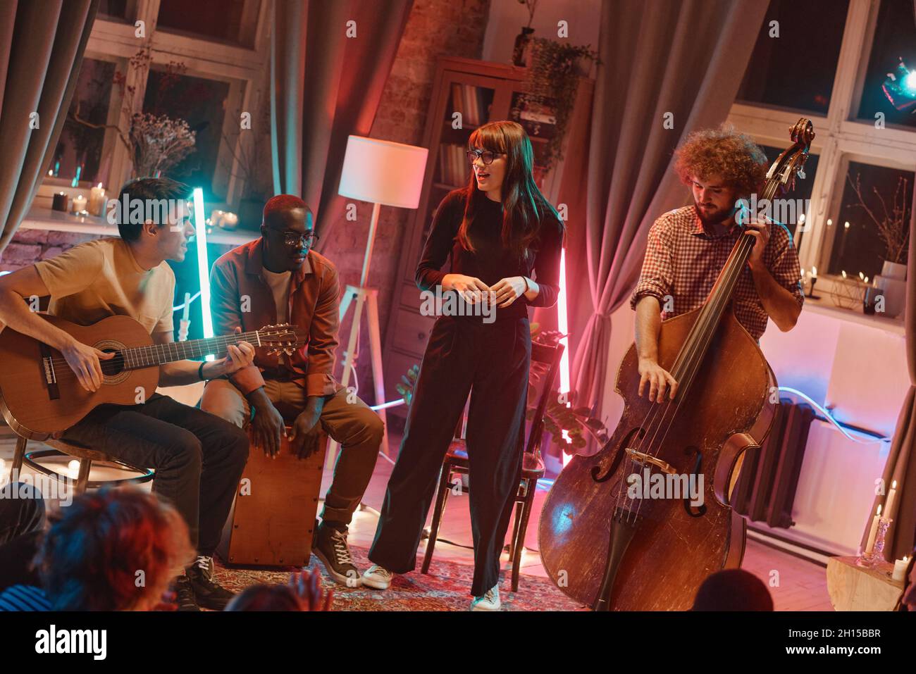 Junge Frau singt, während ihre Band während ihres Aufführens im Club Musikinstrumente spielt Stockfoto