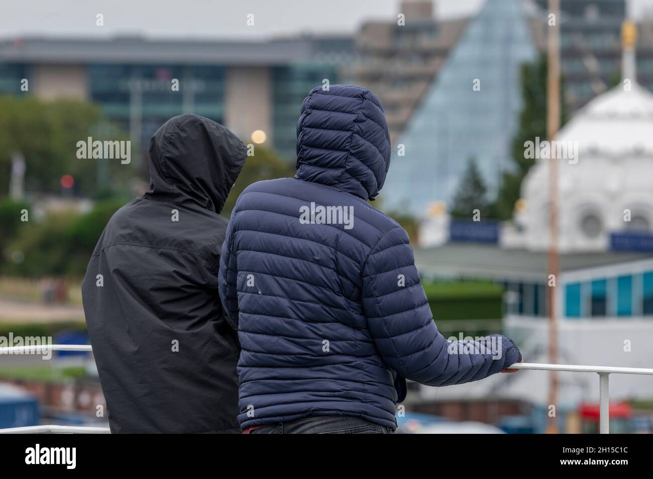 2 Männer oder Jugendliche, die Kapuzenjacken oder Kapuzenmäntel tragen. Verdächtig, bedrohlich, verkleidet, versteckte Gesichter, Verbrechen, Versteckte Gesichter, Kapuzenjacken, Kapuzenpullover. Stockfoto