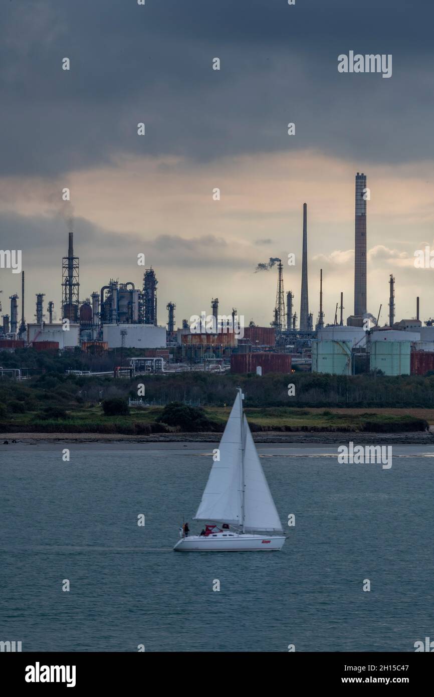 Segelyacht, die an der fawley-Ölraffinerie oder petrochemischen Verarbeitungsanlage auf der southampton-Wasseryacht mit der fawley-Ölraffinerie im Hintergrund vorbeifährt Stockfoto