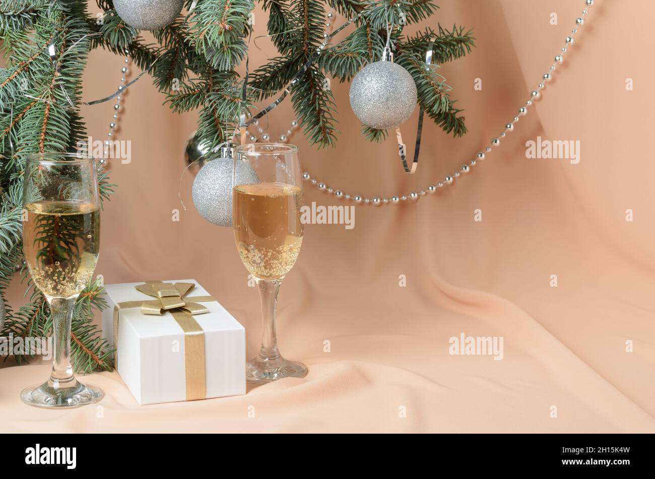 Weihnachten. Eine Neujahrskomposition aus Zweigen eines Weihnachtsbaums, verziert mit silbernen Kugeln, einer Geschenkbox, Sektgläsern auf einer Backgrou Stockfoto