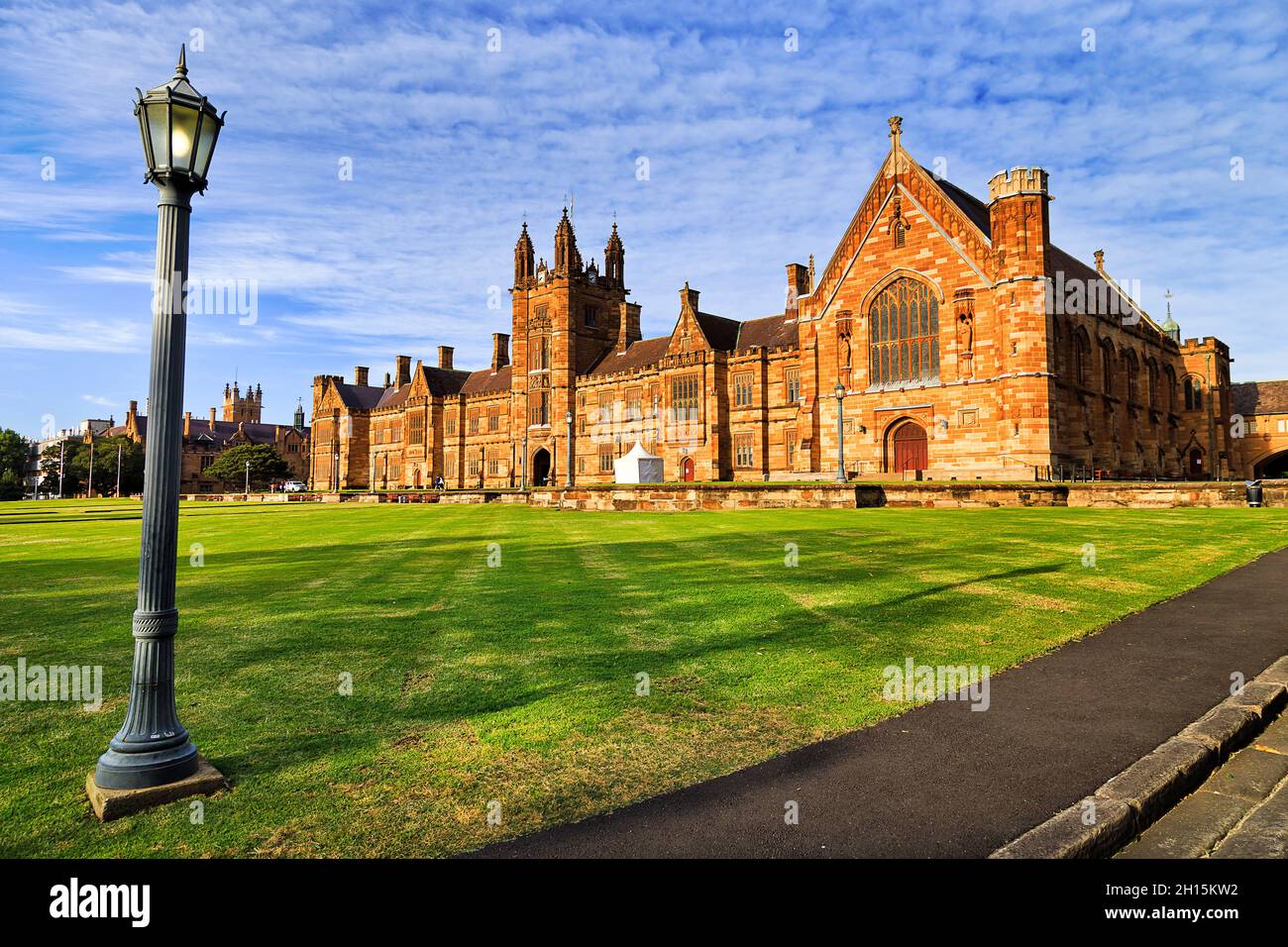 Straßenbeleuchtung auf einem grünen Rasen im Bildungsviertel mit historischen gotischen Gebäuden von Colleges und High-Schools in der City of Sydney. Stockfoto