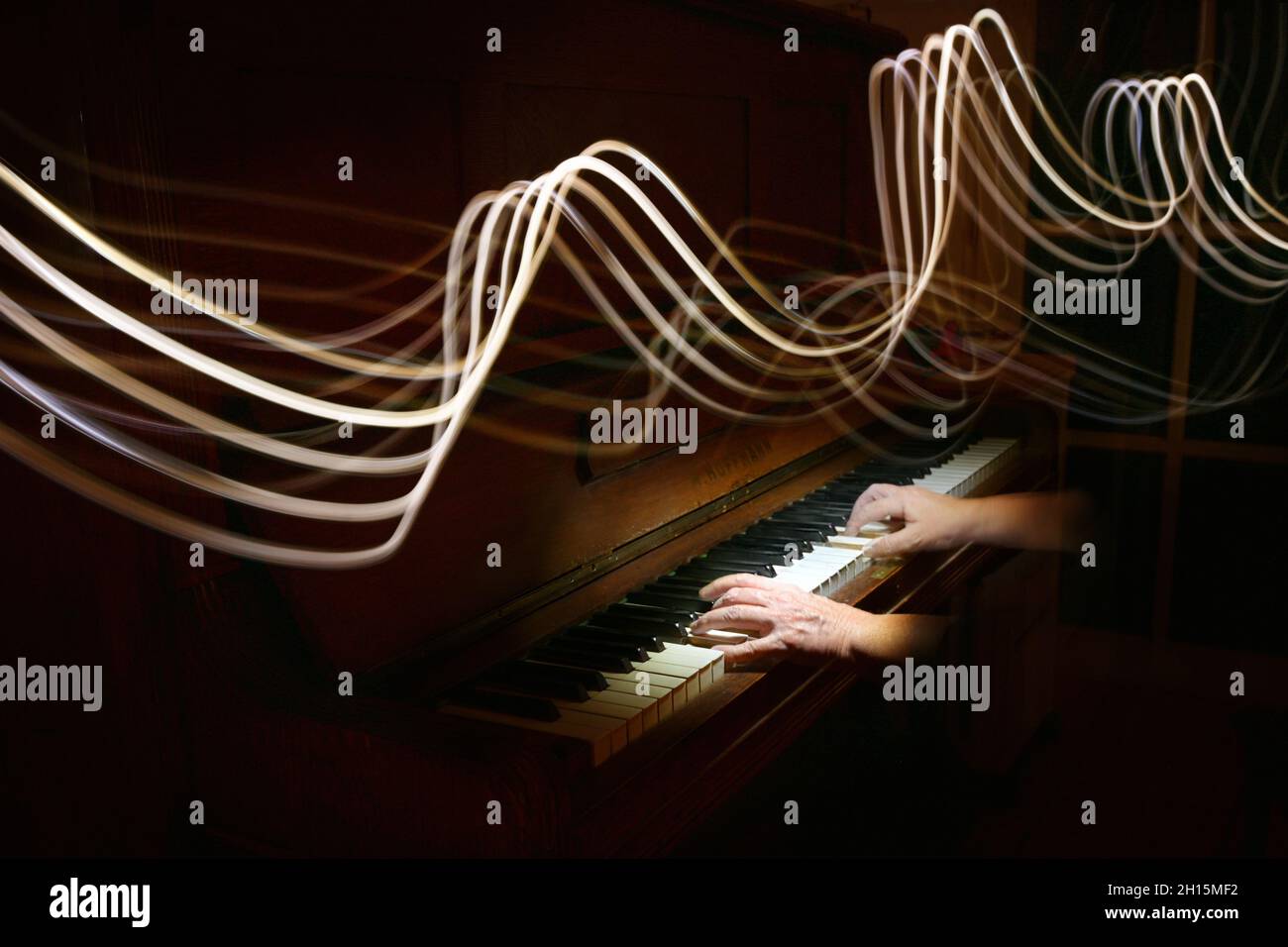 Helle Malerei in Form von geschwungenen Stablinien über den Händen, die auf einem alten Klavier spielen, Musikwellen, dunkler Hintergrund mit Kopierraum, Bewegungsunschärfe, se Stockfoto