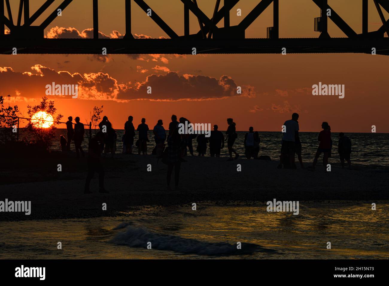 Touristen treffen sich unter der Mackinac Bridge, einer der längsten Brücken der Welt über die Straße von Mackinac, bei Sonnenuntergang, Mackinaw City, Michigan, USA Stockfoto