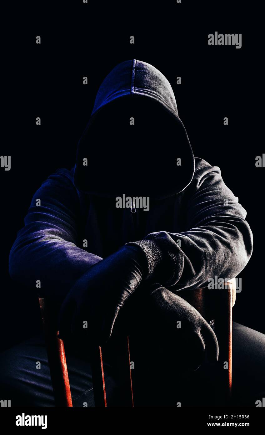 Foto von gruseligen Horror fremden Stalker Mann in schwarzer Kapuze und Kleidung auf Stuhl auf dunklem Hintergrund sitzen. Stockfoto