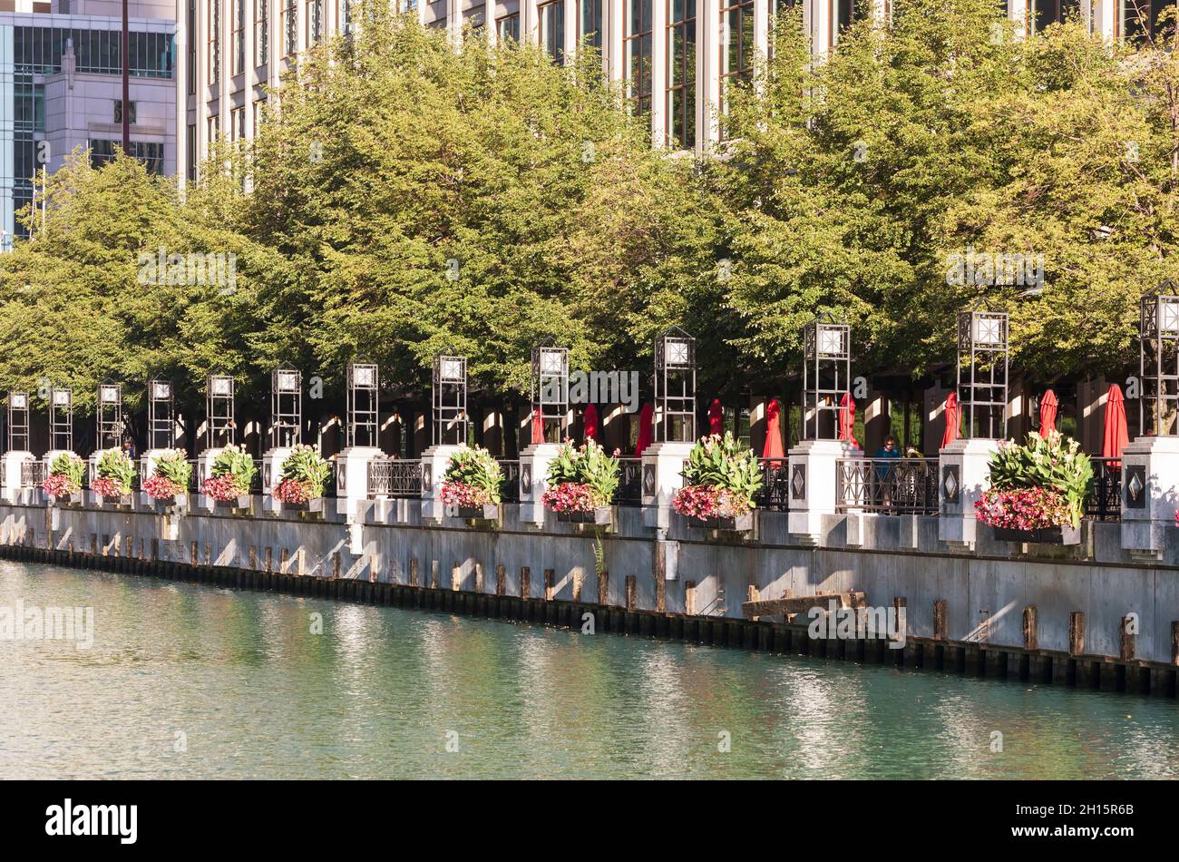 Ein Restaurant am Wasser am Chicago River. Pflanzgefäße mit bunten Blumen schmücken die Geländer am Flussufer. Stockfoto