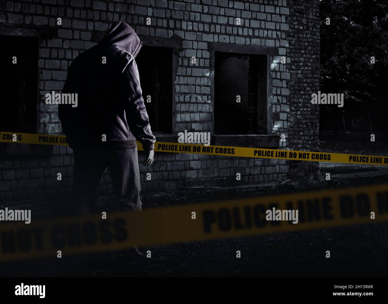 Foto des unheimlichen Horror fremden Stalker Mann in schwarzer Kapuze und Kleidung auf verlassenen Gebäude Hintergrund mit Polizei-Linie Streifen. Stockfoto