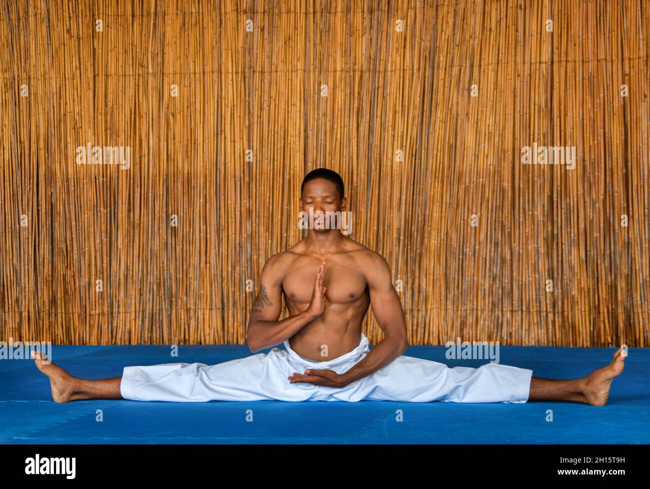 Afrikanische Männer, die bei einem Dojo, einem Wettkampftraining, auf einem blauen Boden eine Spaltung durchmachen Stockfoto