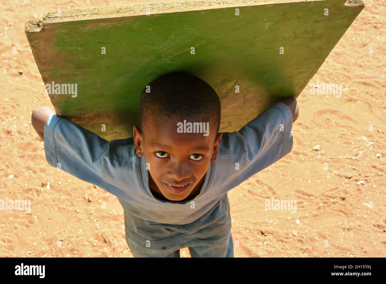 Afrikanisches Kind trägt ein großes und schweres Stück Holz Stockfoto