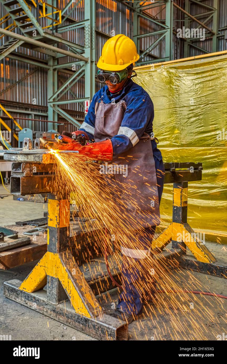 Afrikanische Arbeiterin mit roten Handschuhen, die in einer Stahlfabrik in Botswana-Afrika mit einer Fackel in der Ecke Metall schneidet Stockfoto