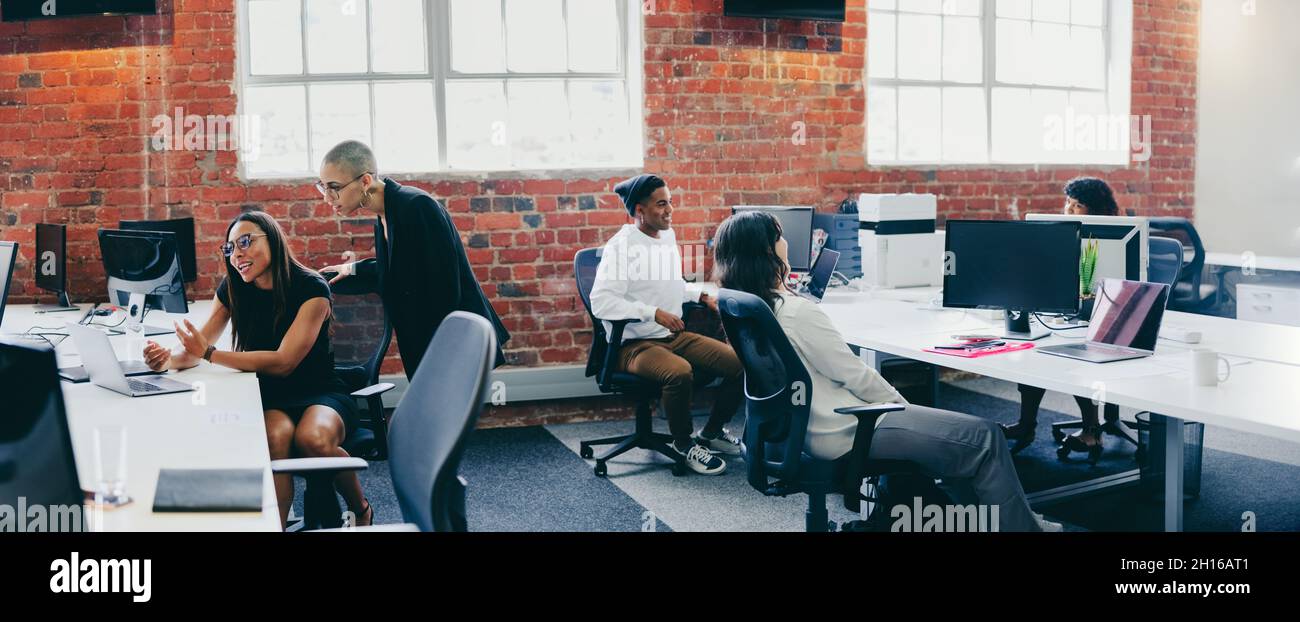 Geschäftsleute, die an einem kreativen, modernen Arbeitsplatz arbeiten. Gruppe junger Geschäftsleute, die miteinander interagieren, während sie an ihren Schreibtischen sitzen. Colleag Stockfoto