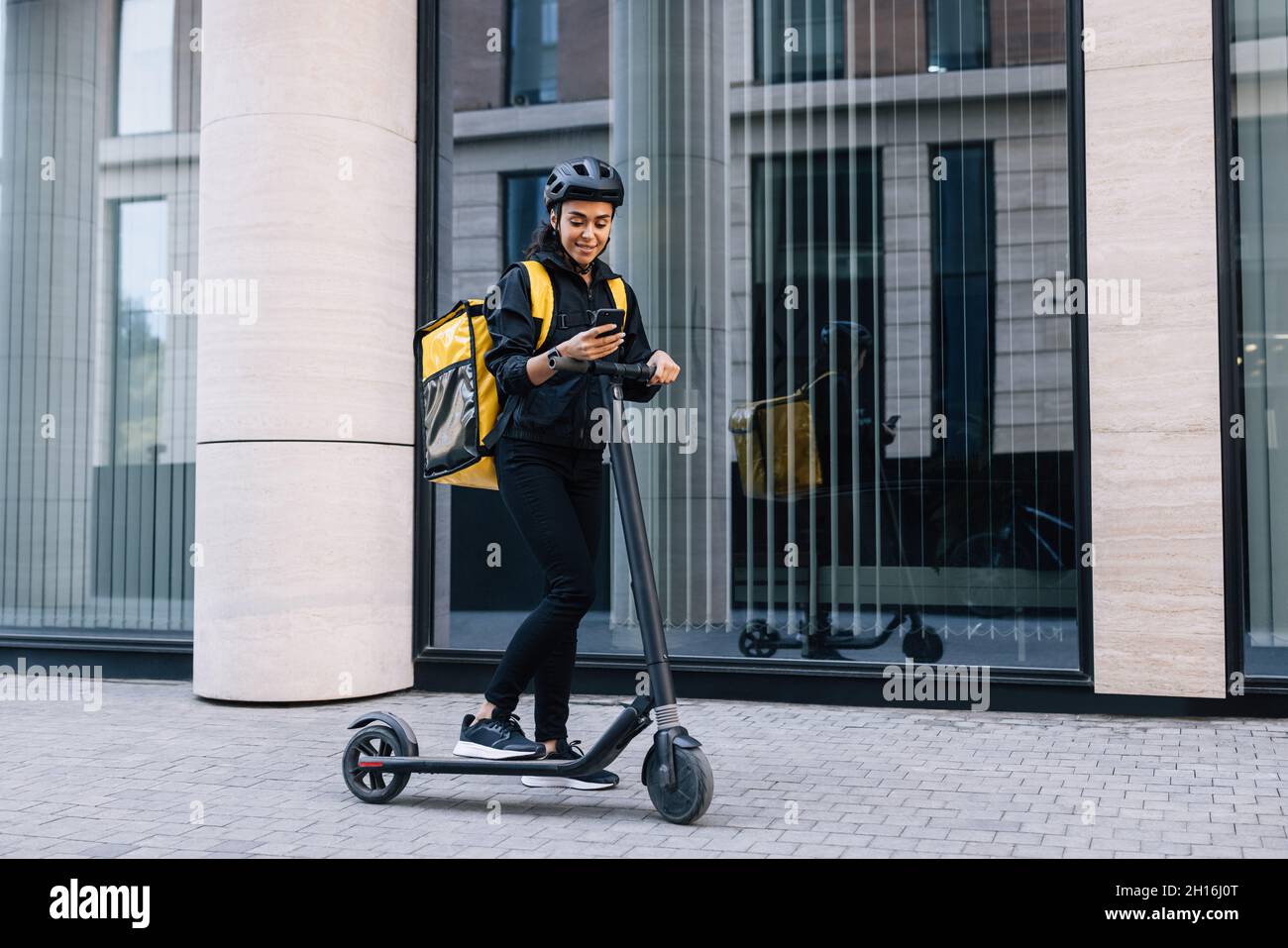 Delivery Frau mit Smartphone, während in der Stadt mit Elektro-Push-Scooter stehen Stockfoto