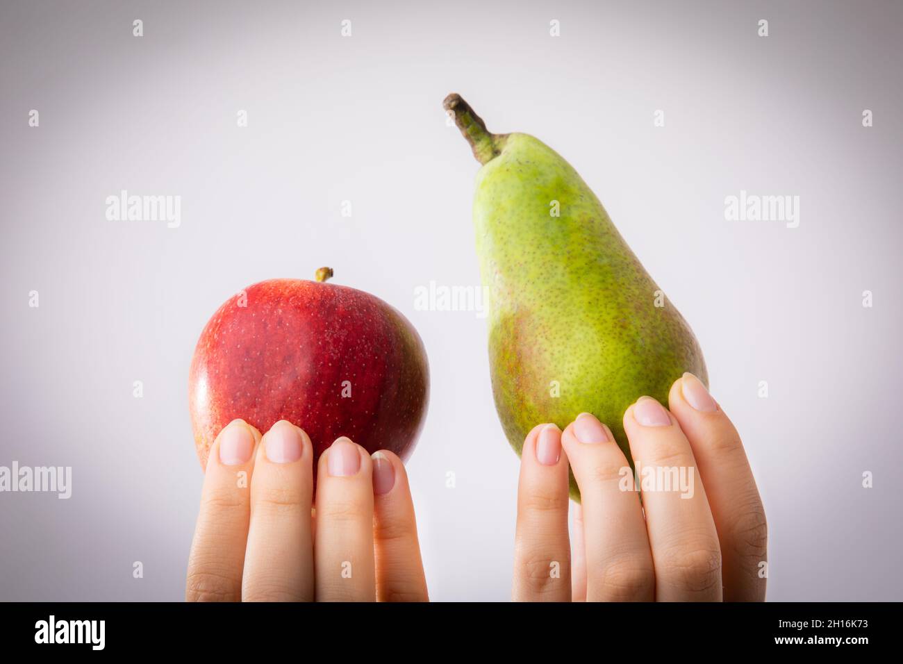 Roter und grüner Apfel und Birne in weiblichen Händen gehalten. Konzeptionell für Vergleich, Differenzierung und Auswahlverfahren. Stockfoto