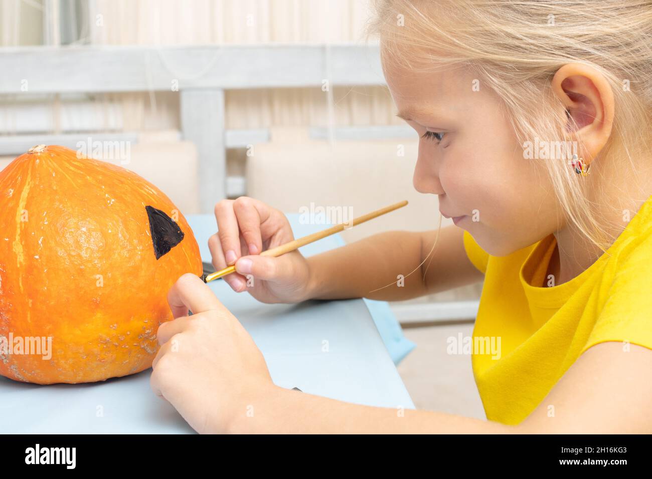 Das Mädchen kreiert eine Laterne aus einem Kürbis, die zu Hause am Tisch in der Küche sitzt. Halloween-Party und Familie Lifestyle Hintergrund Stockfoto