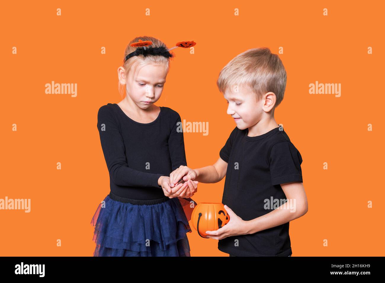 Halloween Kinder. Kindertrick oder -Genuss ist eine Halloween-Tradition. Junge und Mädchen halten einen orangefarbenen Kürbis-förmigen Korb mit Leckereien in den Händen Stockfoto