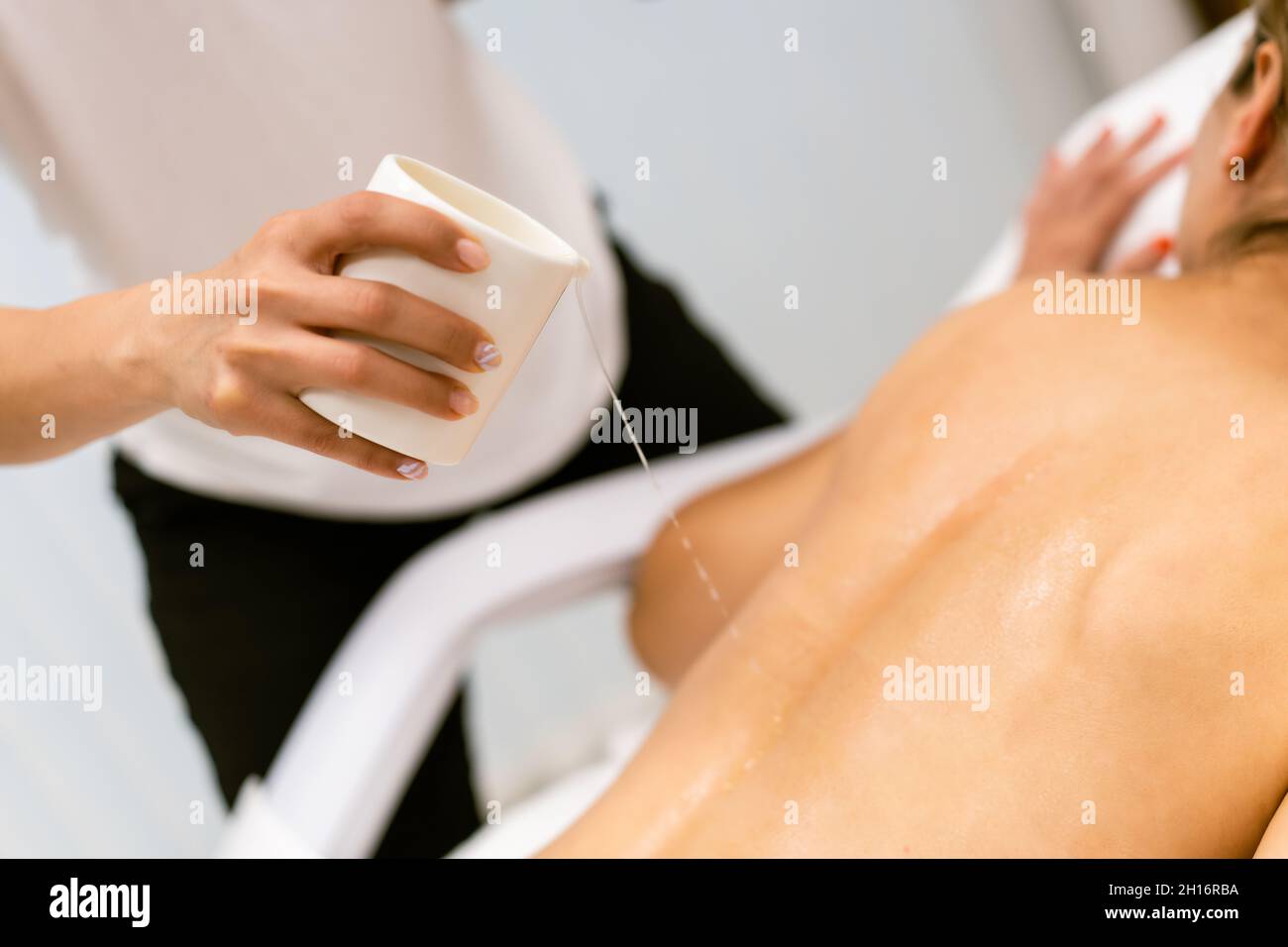 Der professionelle Schönheitssalon gießt Öl aus einer Massagekerze auf den Rücken seines Patienten. Stockfoto