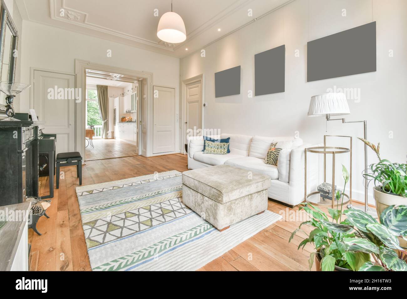 Interieur des klassisch gestalteten Wohnzimmers mit komfortablem Sofa in der Nähe der Fenster vor dem Klavier und Kamin in hellen geräumigen Wohnung platziert Stockfoto