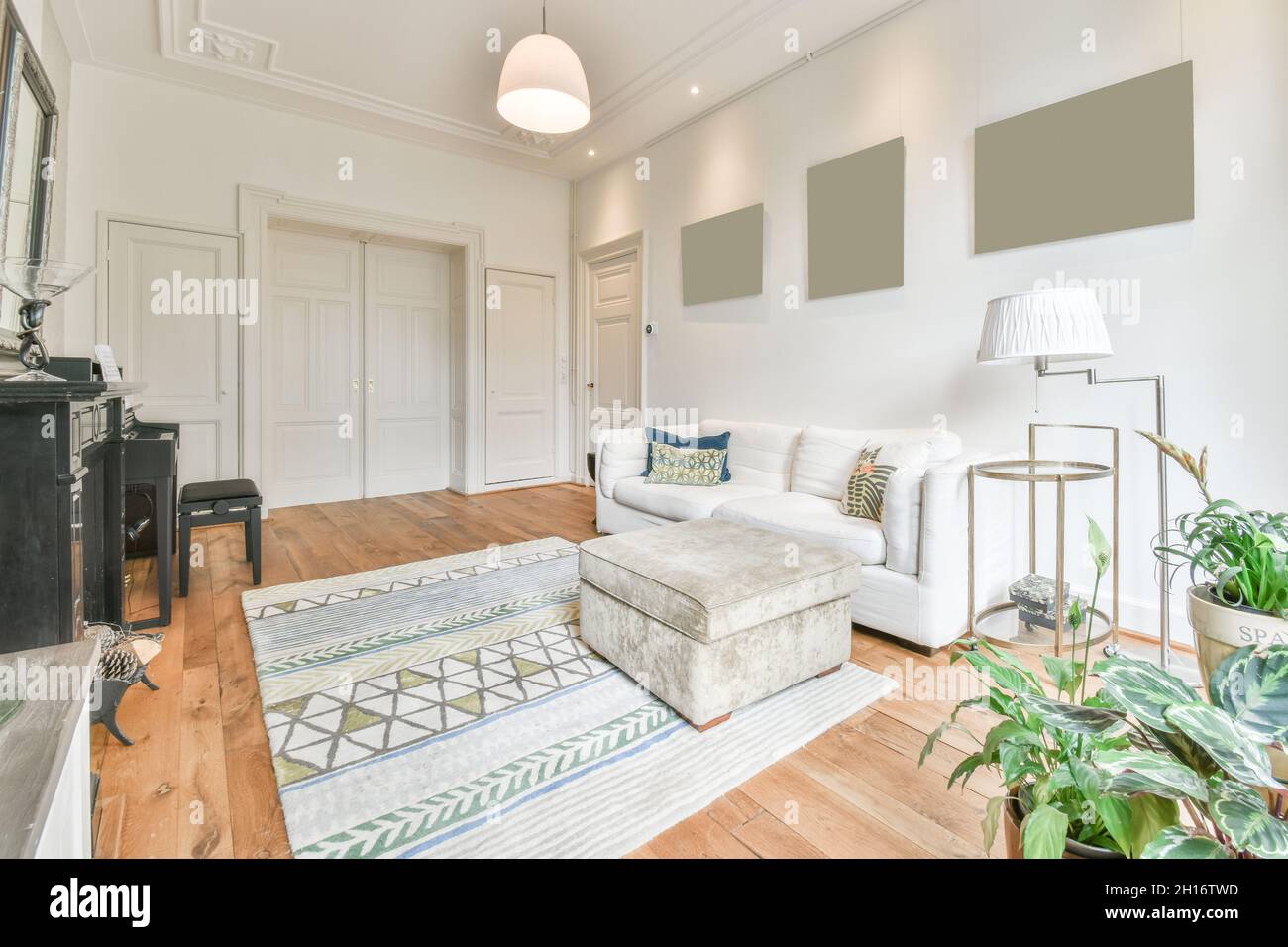 Interieur des klassisch gestalteten Wohnzimmers mit komfortablem Sofa in der Nähe der Fenster vor dem Klavier und Kamin in hellen geräumigen Wohnung platziert Stockfoto