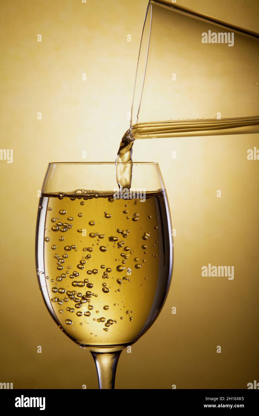 Gießen Sie Weißwein aus einer Karaffe in ein Glas Stockfoto